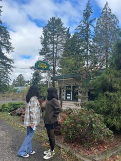 two people standing in front of a small cabin on the side of a dirt road