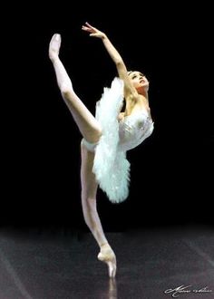 a ballerina in white tutu and feathered skirt doing a ballet move with her arms stretched out