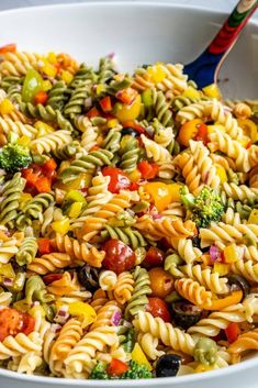 a pasta salad with broccoli, tomatoes and olives in a white bowl