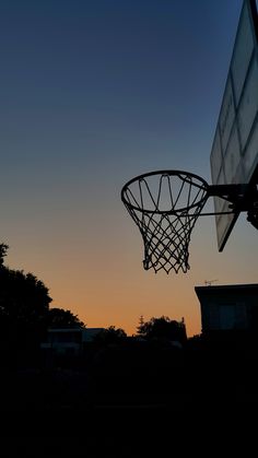 a basketball hoop is silhouetted against the evening sky as the sun sets in the distance