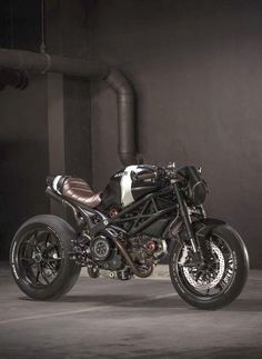 a black and white motorcycle parked in front of a dark room with pipes on the wall