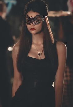 a woman in a black dress with a mask on her face and long dark hair