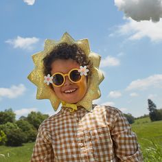 a young boy wearing sun glasses and a fake flower on his head in the grass