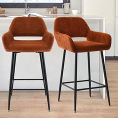 two brown chairs sitting next to each other on top of a wooden floor in front of a white counter