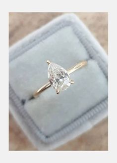 an engagement ring with a pear shaped diamond in it on a velvet box that is sitting on the floor