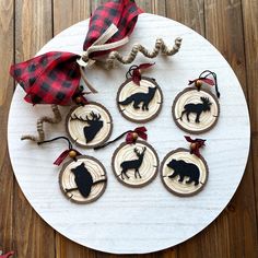 wooden ornaments with black silhouettes of deer and moose on them are sitting on a white plate