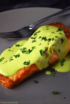 a piece of salmon covered in green sauce on a plate with a fork next to it