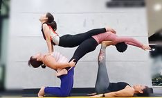 two women doing yoga poses in front of a gray wall, with one holding the other upside down