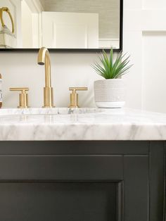 a bathroom sink with marble counter top and gold faucet, mirror above it