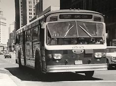 a black and white photo of a bus driving down the street in front of tall buildings