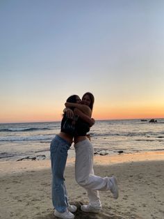 two women hugging each other on the beach at sunset with waves in the background and one woman wearing white boots