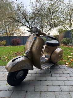 an old scooter is parked on the sidewalk in front of some trees and grass