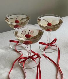 two martini glasses with cherries on the rims and ribbons tied around them, sitting on a table