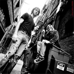 black and white photograph of three young men standing on the side of a building with their skateboards