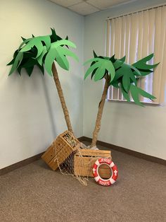 two palm trees made out of cardboard boxes in an office cubicle with a life preserver on the floor