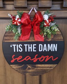 a wooden sign that says tis the damn season hanging on a door with red bows