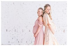 two women standing next to each other in front of a white brick wall wearing dresses