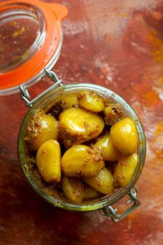 a glass jar filled with pickled potatoes on top of a wooden table next to an orange lid