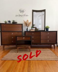 a wooden dresser sitting on top of a hard wood floor next to a red sold sign