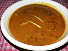 a white bowl filled with soup sitting on top of a checkered tablecloth covered table