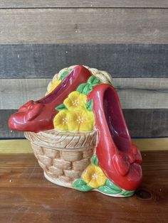 a red shoe sitting on top of a basket next to a wooden wall with flowers