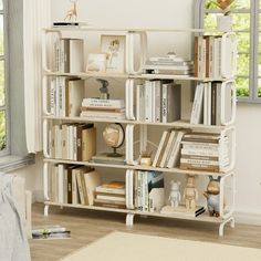 a white book shelf filled with books in a room next to a window and rug