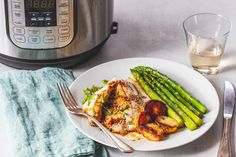 a white plate topped with chicken and asparagus next to an instant pressure cooker