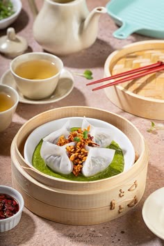 a table topped with plates and bowls filled with food next to tea cups, sauces and chopsticks