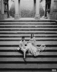 black and white photograph of two people sitting on steps in front of stairs, one holding the other's hand