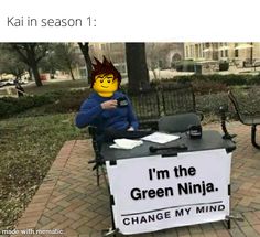 a person sitting at a table with a sign on it that says i'm the green ninja change my mind