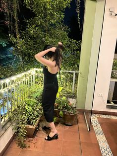 a woman in black dress standing on balcony next to potted plants