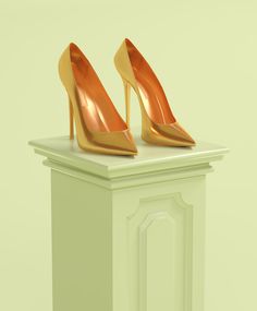 a pair of gold high heeled shoes sitting on top of a white pedestal