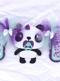 a panda bear cut out with purple and green bows on it's head, sitting next to two cell phones