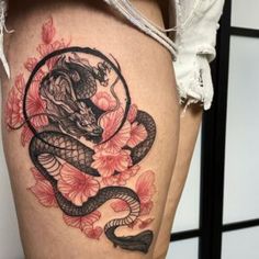 a woman's thigh with a snake and flowers tattoo design on it, sitting next to a wall