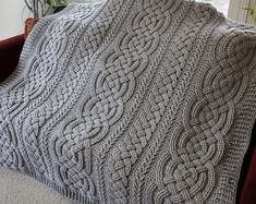 a gray knitted blanket sitting on top of a red couch next to a window