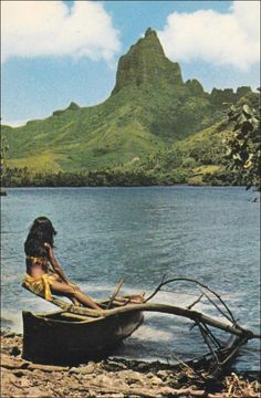 a woman sitting in a boat on top of a lake next to a lush green mountain