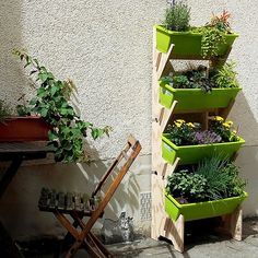 a wooden planter with plants in it next to a chair on the ground and a wall behind it