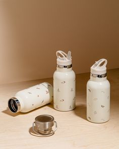 two white water bottles sitting on top of a wooden table next to a silver cup