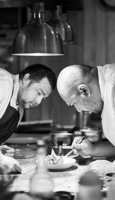 two men in the kitchen preparing food on a plate with utensils and spoons