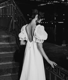 black and white photograph of woman in evening dress looking down the stairs at city lights