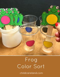 the frog color sort is being held up in front of three cups with stickers on them