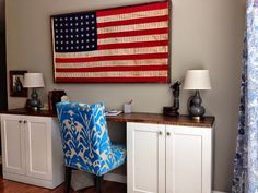 an american flag hanging on the wall above a desk with a blue and white chair