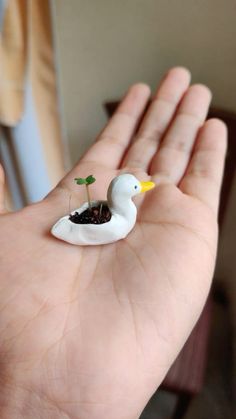 a hand holding a tiny white bird with a plant in it's beak,