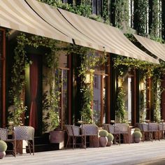 an outdoor restaurant with tables and chairs covered in plants on the side of the building