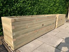 a large wooden planter sitting on top of a cement floor next to a lush green bush