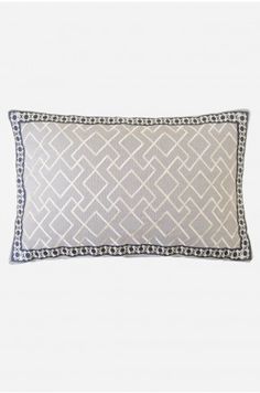 a gray and white pillow with an embroidered border on the front, sitting against a white wall