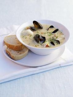 a white plate topped with a bowl of soup next to a slice of bread on top of a napkin