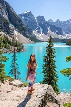 a woman standing on the edge of a cliff overlooking a lake with mountains in the background