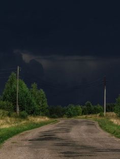 an empty dirt road under a dark sky