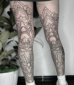 a woman's legs with black and white tattoos on them, in front of a potted plant